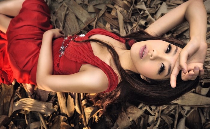 Asian woman in red dress lying on dried leaves