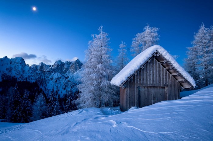 Wooden hut in snowy mountains under moonlight