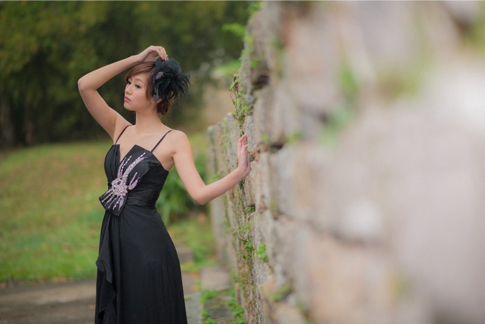 Woman in black dress posing by stone wall