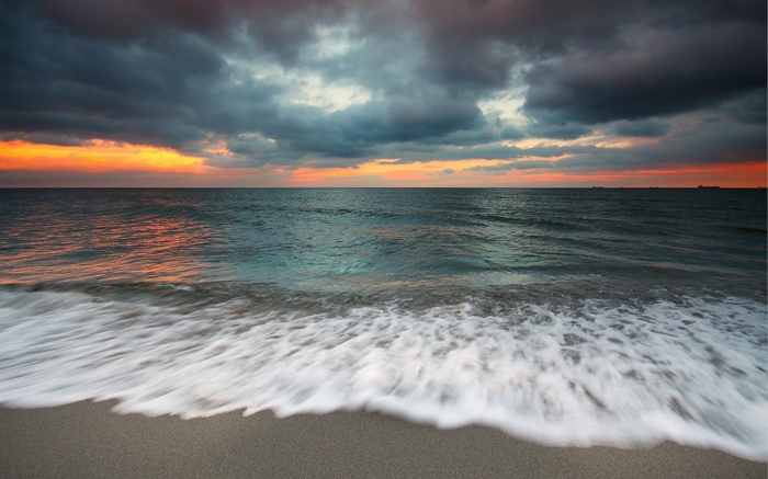 Ocean waves crashing on a sandy beach at sunset
