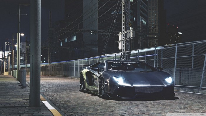 Gray Lamborghini Aventador parked on a cobblestone street at night