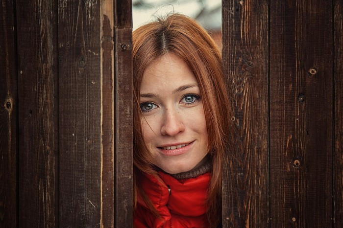Woman with red hair peeking through wooden fence