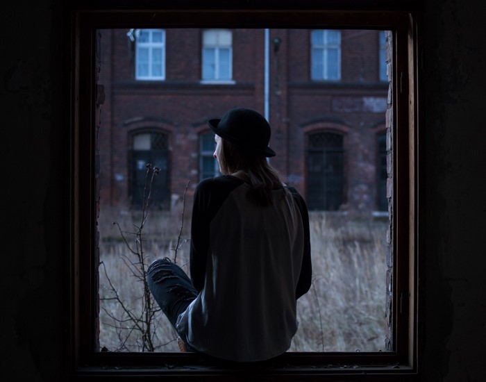 Person in hat looking out a broken window