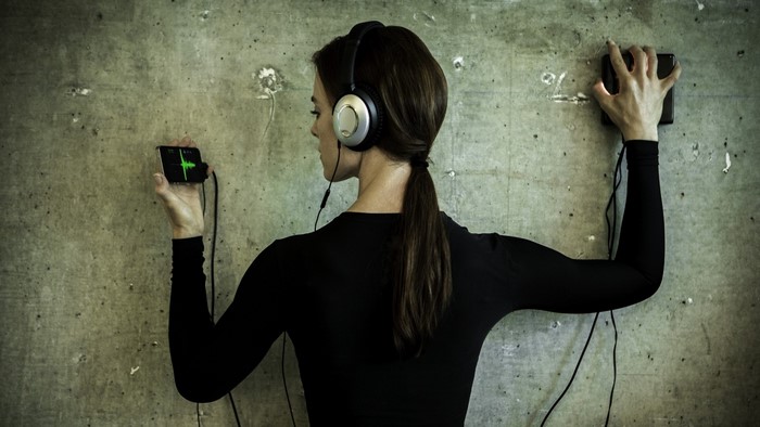 Woman with headphones listening to sound on phone against wall