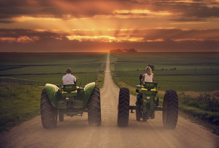 Two tractors driving on a dirt road at sunset