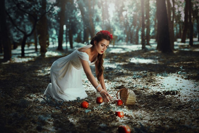 Woman in white dress picking apples in a forest
