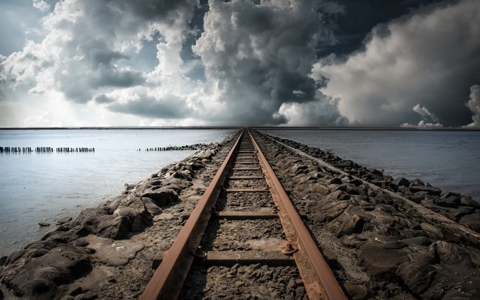 Railway tracks leading into the sea under dramatic clouds