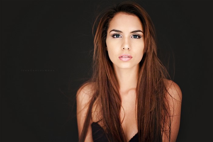 Woman with long brown hair posing against a dark background
