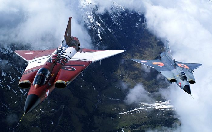 Two fighter jets flying over mountains