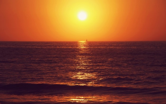Sunset over the ocean with a sailboat