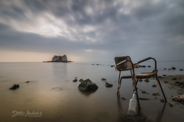 Rusty chair and bottle on a rocky shore with island in the sea
