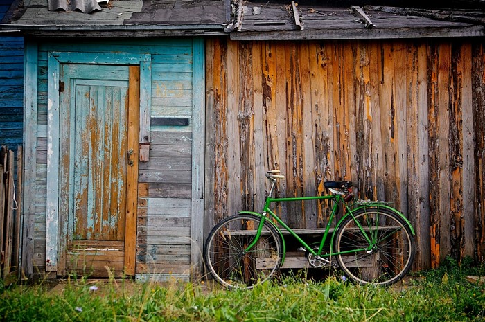 Green bicycle leaning against a weathered wooden wall with a blue door