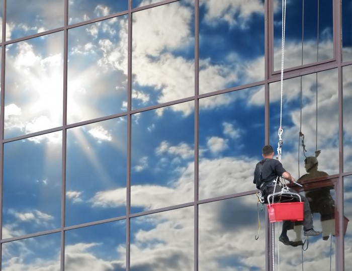 Window cleaner working on a skyscraper reflecting the sky