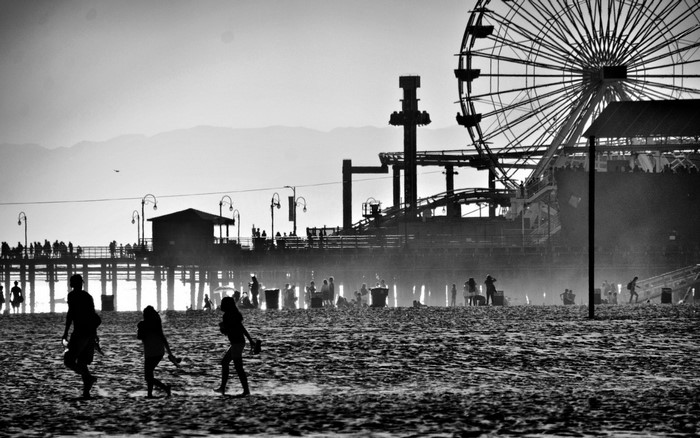People on a beach with a pier and Ferris wheel