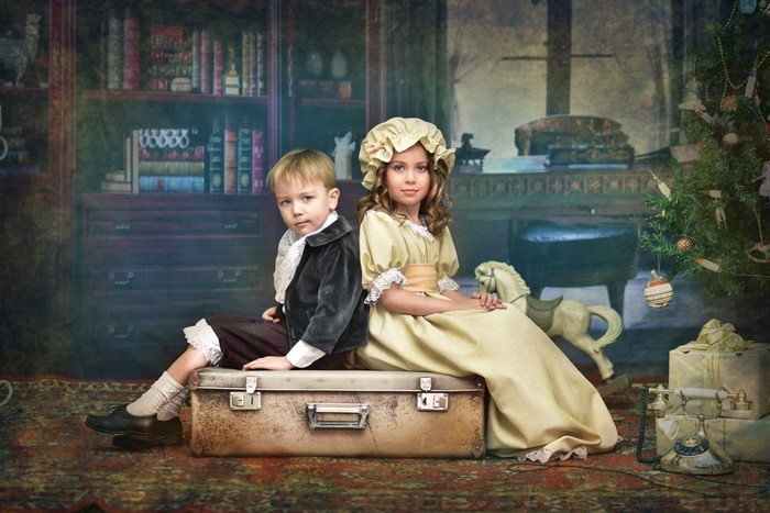 Children in vintage clothing sitting on a suitcase