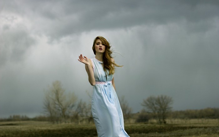 Woman in a light blue dress in a field under a stormy sky