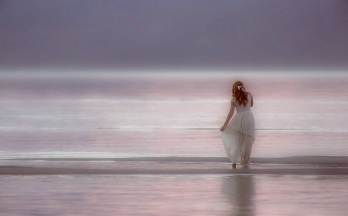 Woman in white dress on a misty beach at sunrise