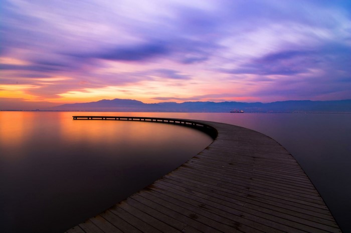 Wooden pier on a calm sea during sunset with purple clouds