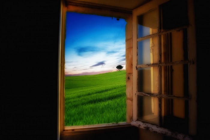 View through an open window of a green field and sky