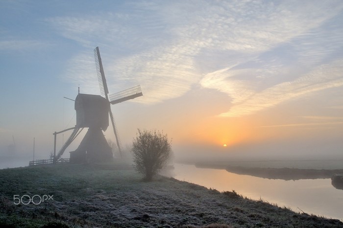 Windmill in the mist at sunrise with a river