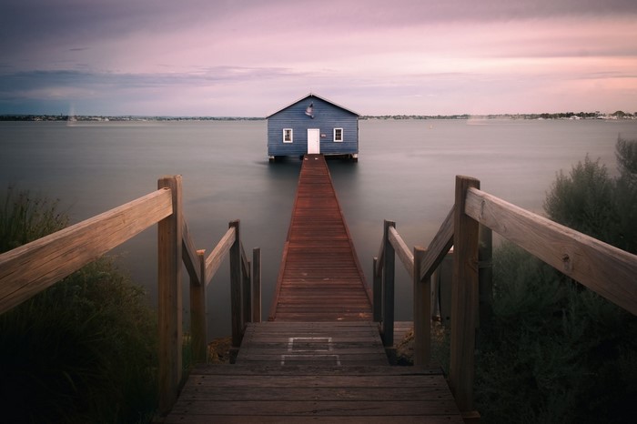Blue boathouse on a calm lake at sunset with wooden pier