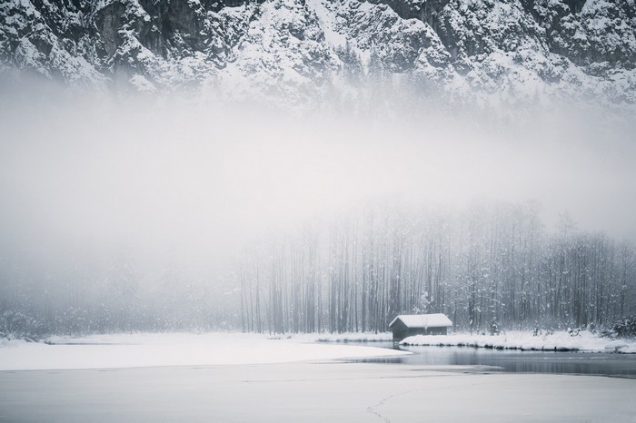 Snowy mountain landscape with a cabin by a misty lake
