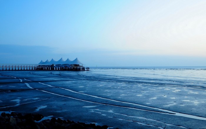 White tents on a pier over a muddy shore at dawn
