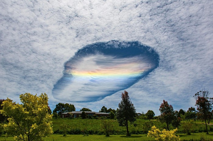 Fallstreak hole with rainbow in clouds over rural landscape