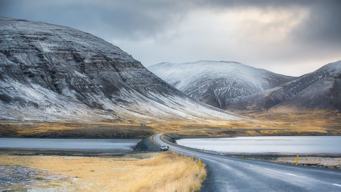 Car on a road through snowy mountains and a lake