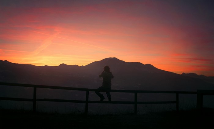 Silhouette of a person sitting on a fence at sunset