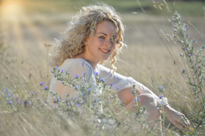 Woman with curly blonde hair sitting in a field
