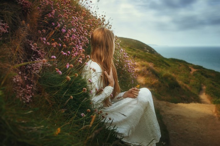 Woman in white dress sitting by flowers overlooking the sea