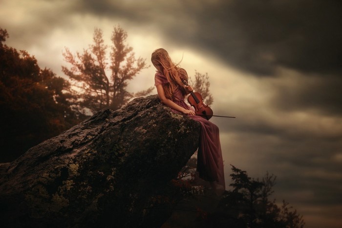 Woman with violin sitting on a rock at sunset
