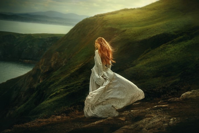 Woman in white dress on a grassy cliff overlooking the sea