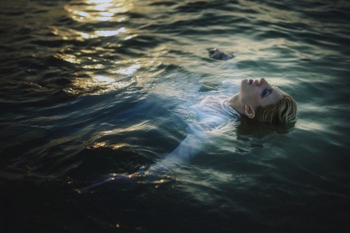 Woman floating in dark water with sunlight reflection