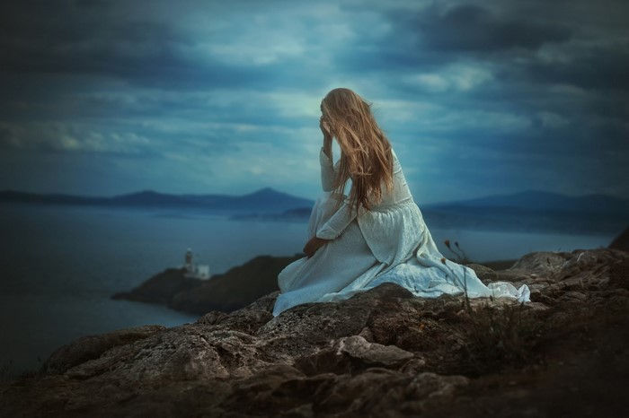 Woman in white dress on rocky coast overlooking sea