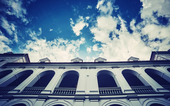 White building with arched windows against a blue sky with clouds