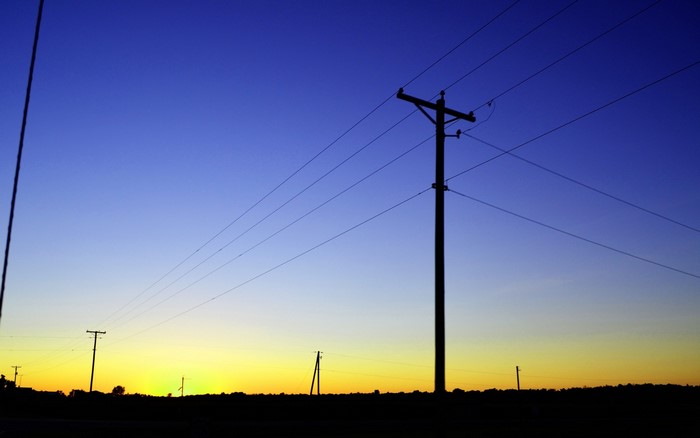 Silhouette of utility poles and power lines against a sunset sky