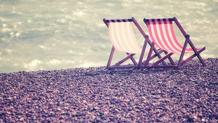Two deck chairs on a pebble beach by the sea