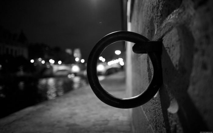 Monochrome night scene with a ring on a wall by a canal