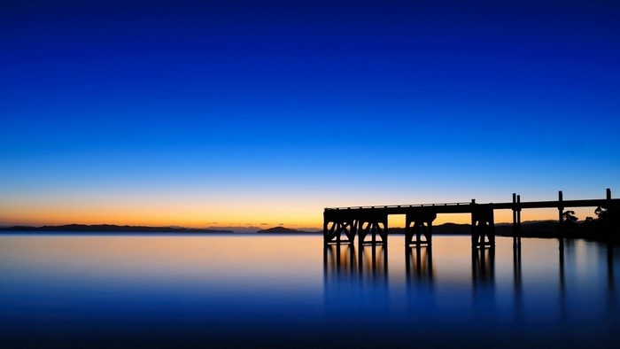 Pier over calm water at dusk with mountain horizon