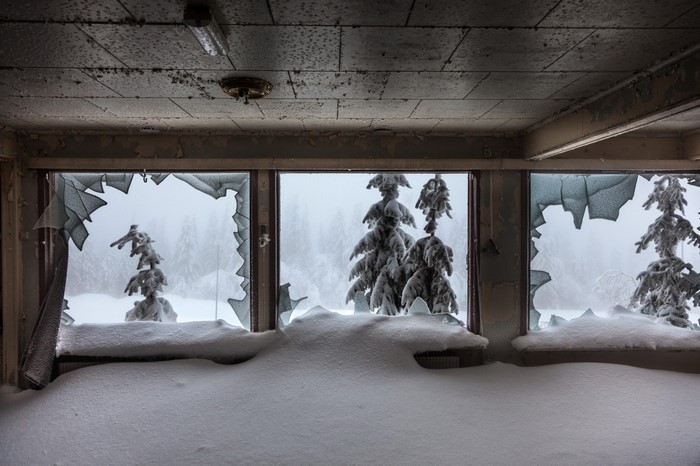 Abandoned building interior with broken windows and snow-covered trees