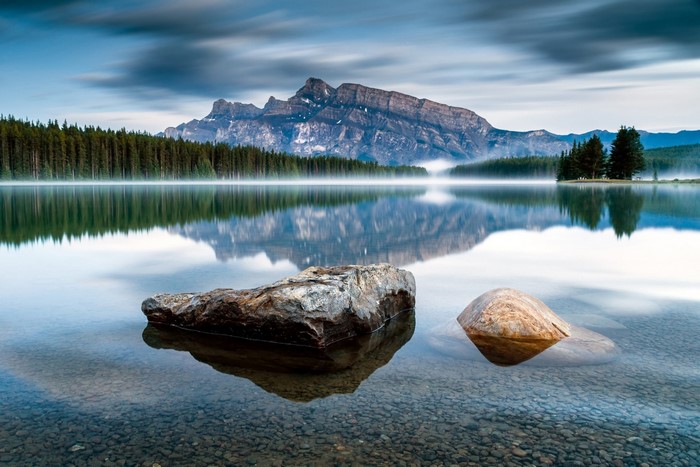 Misty lake with rocky shore and mountain reflection