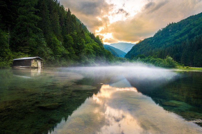 Misty lake with a boathouse and forested mountains