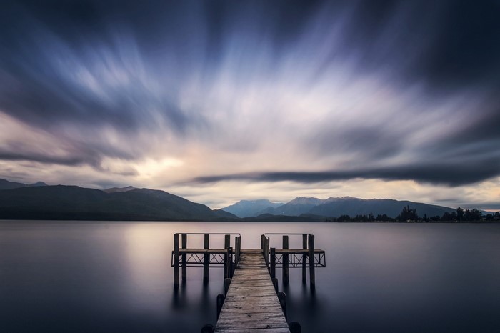Wooden pier on a calm lake with mountains and dramatic clouds