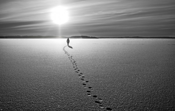 Person walking on frozen lake with sun and footprints