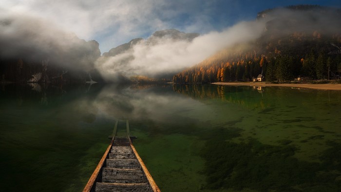 Wooden walkway on a misty lake with mountains