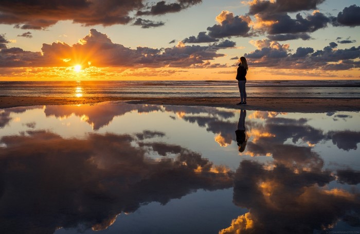 Person watching sunset over the ocean with reflection