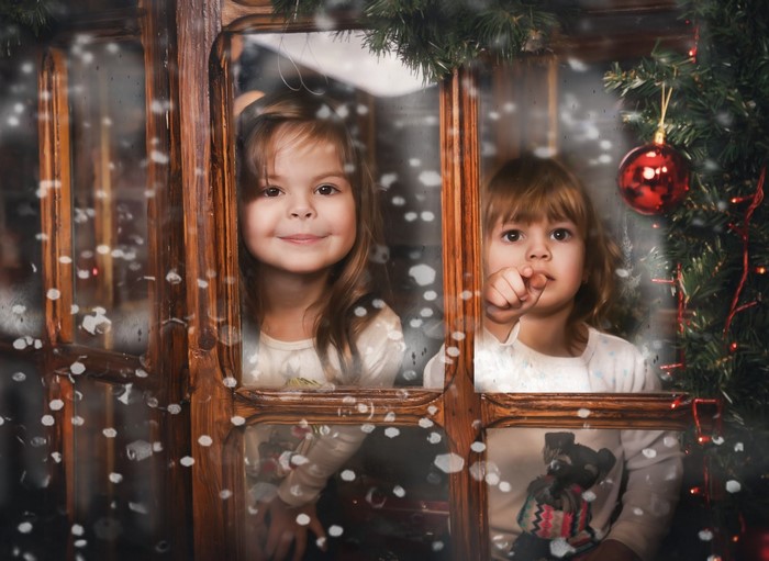 Two young girls looking out a window during winter