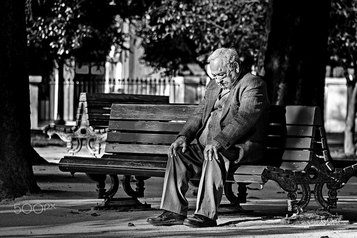 Elderly man sitting on a park bench in black and white